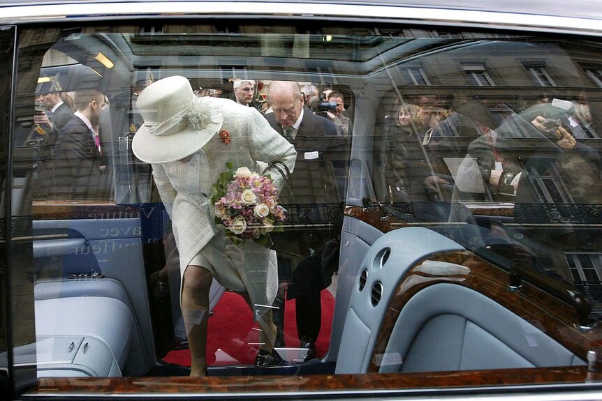 A photo of Queen Elizabeth II and Prince Philip entering a car, taken through the window.