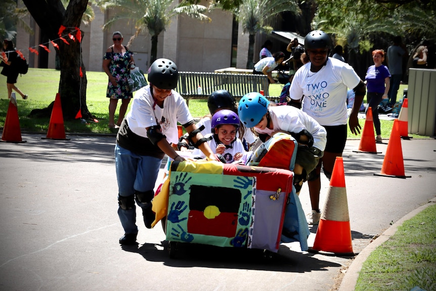 kids push a girl on a couch decorated with the aboriginal flag
