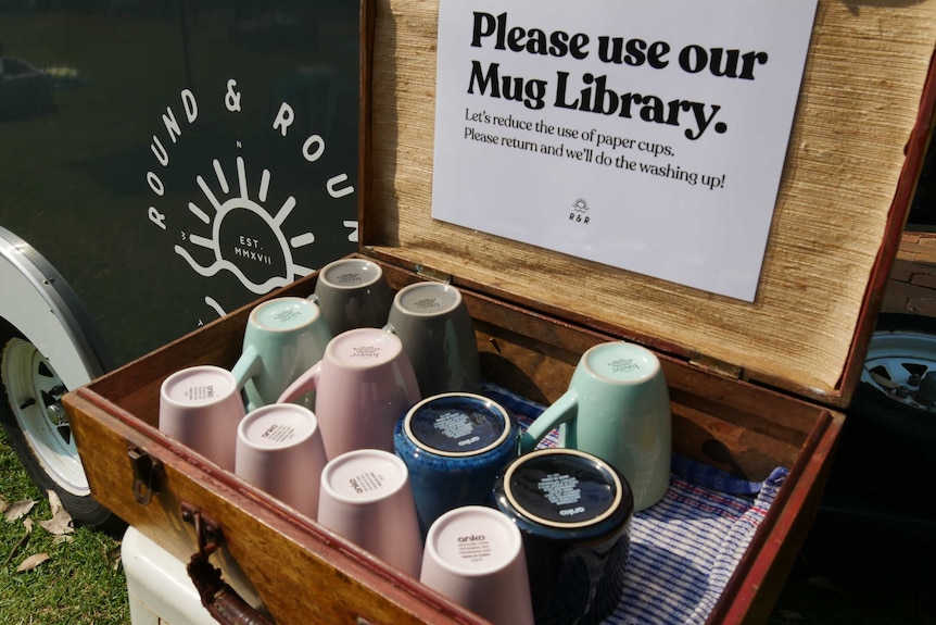A case holding coffee cups with a sign saying 'please use our mug library'.