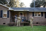 Two army personnel standing outside a brick home. 
