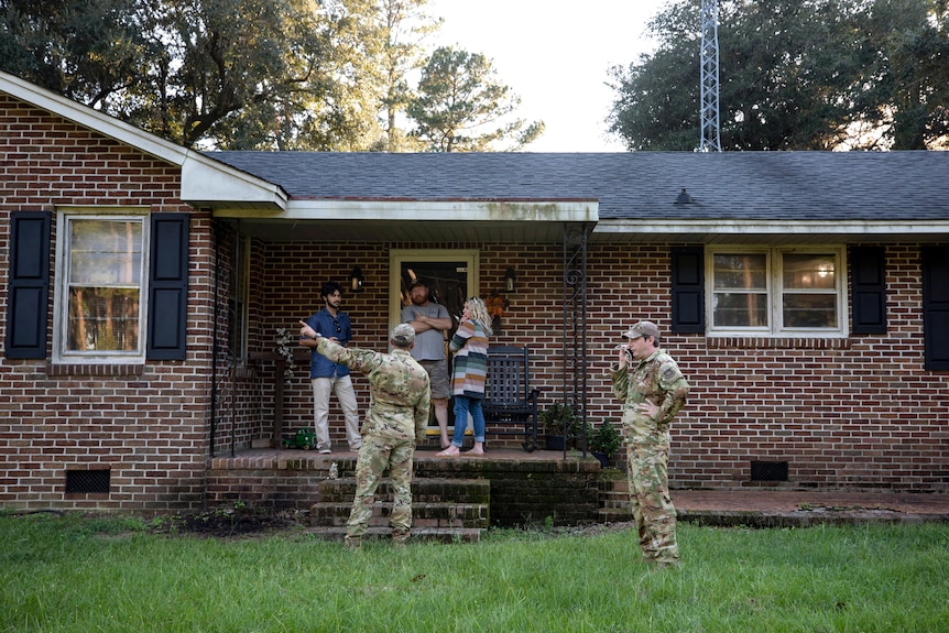 Two army personnel standing outside a brick home. 