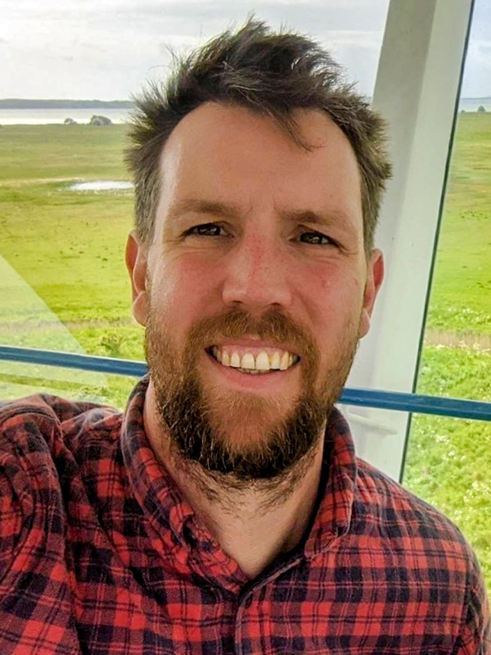 A man smiling in a selfie wearing a black and red checked flannel