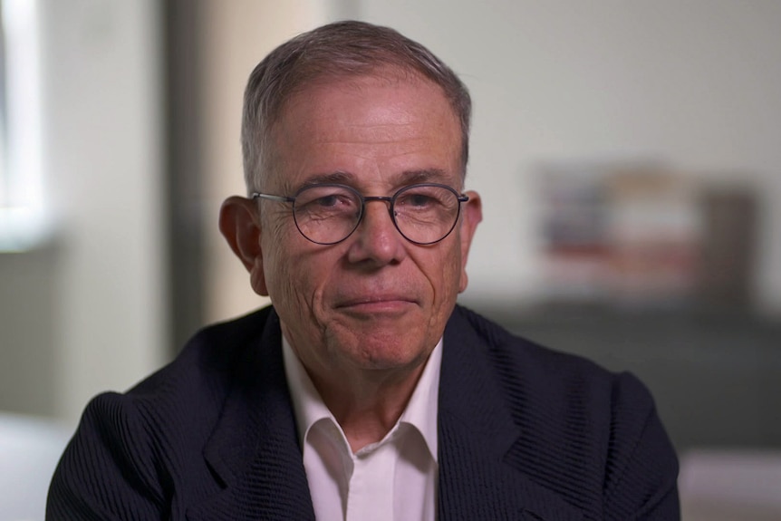 A man wearing glasses, suit jacket and collared shirt.