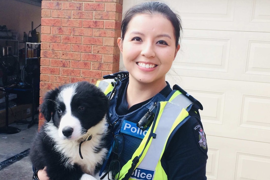 A woman holds a dog while wearing police uniform.