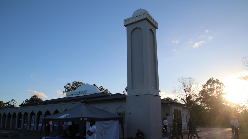 a mosque with a tall tower as the sun sets over the horizon 
