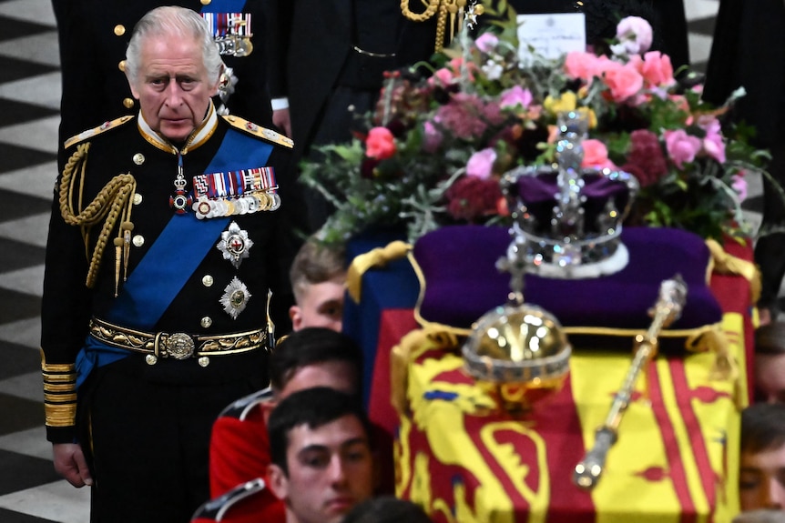 King Charles with a sad expression on his face next to the Queen's coffin. 