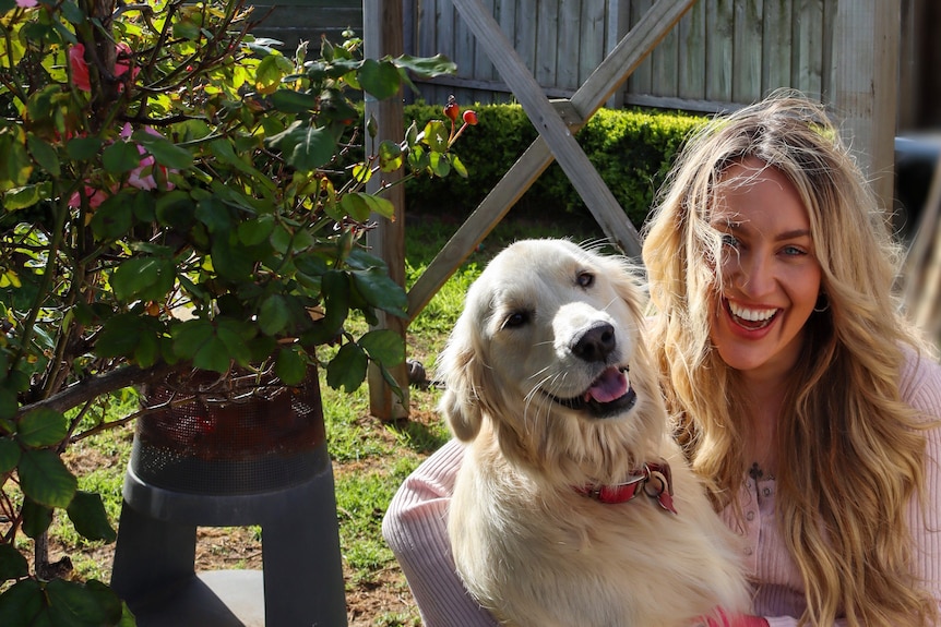 Woman poses with her pet dog in the backyard of her Geelong rental, where she's planted a veggie patch.
