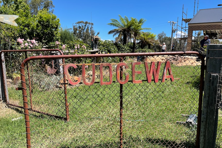 A rusty gate with a garden in the background and a home in the background being rebuilt. 