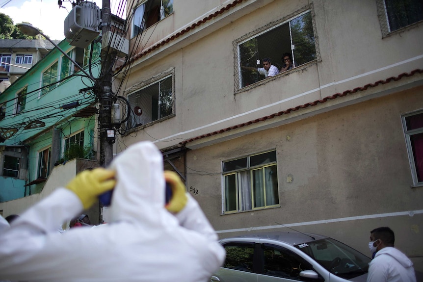 Residents watch water utility workers disinfecting a favela.