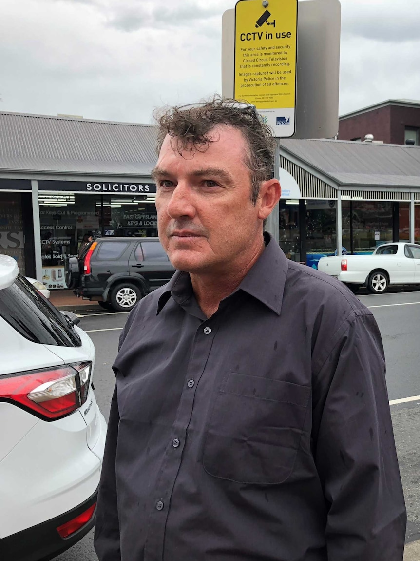 A man with grey curly hair and glasses on his head pictured in front of shops