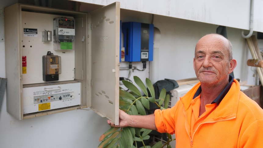 A man in an orange shirt stands next to a meter box.