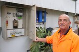 A man in an orange shirt stands next to a meter box.