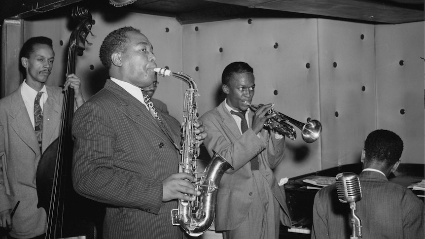 Jazz musicians wearing suits play their instruments on a curtained stage.