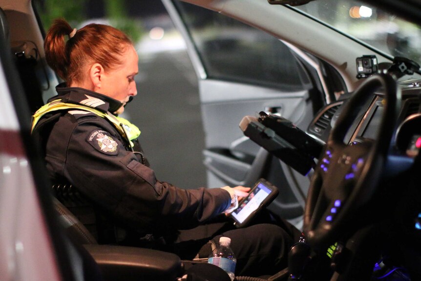 Sergeant Jackie Heath sits in the passenger seat of a police vehicle, using an iPad.