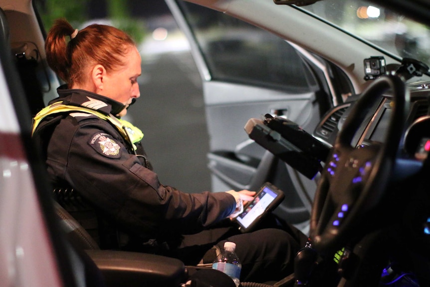 An officer sits in the passenger seat of a police vehicle, using an iPad.