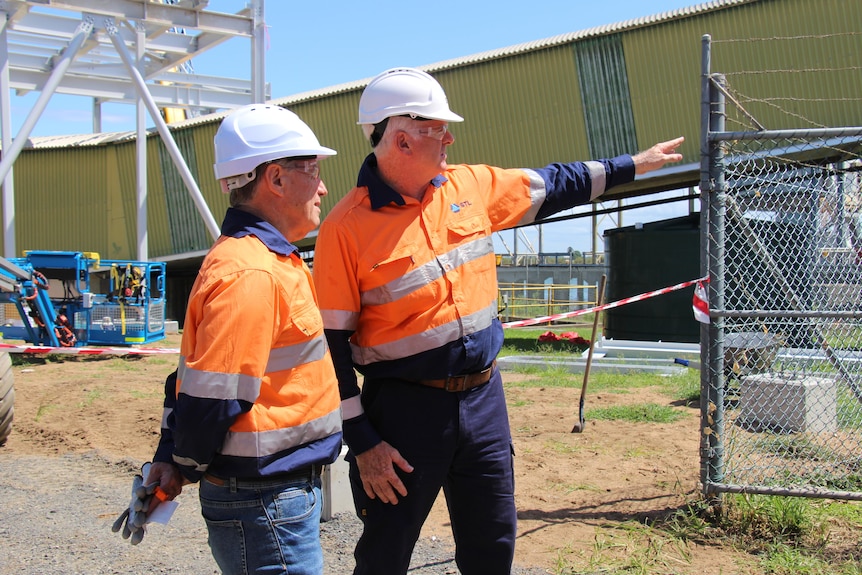 Two men in high-vis uniform shirts and hard hats standing, one pointing off camera