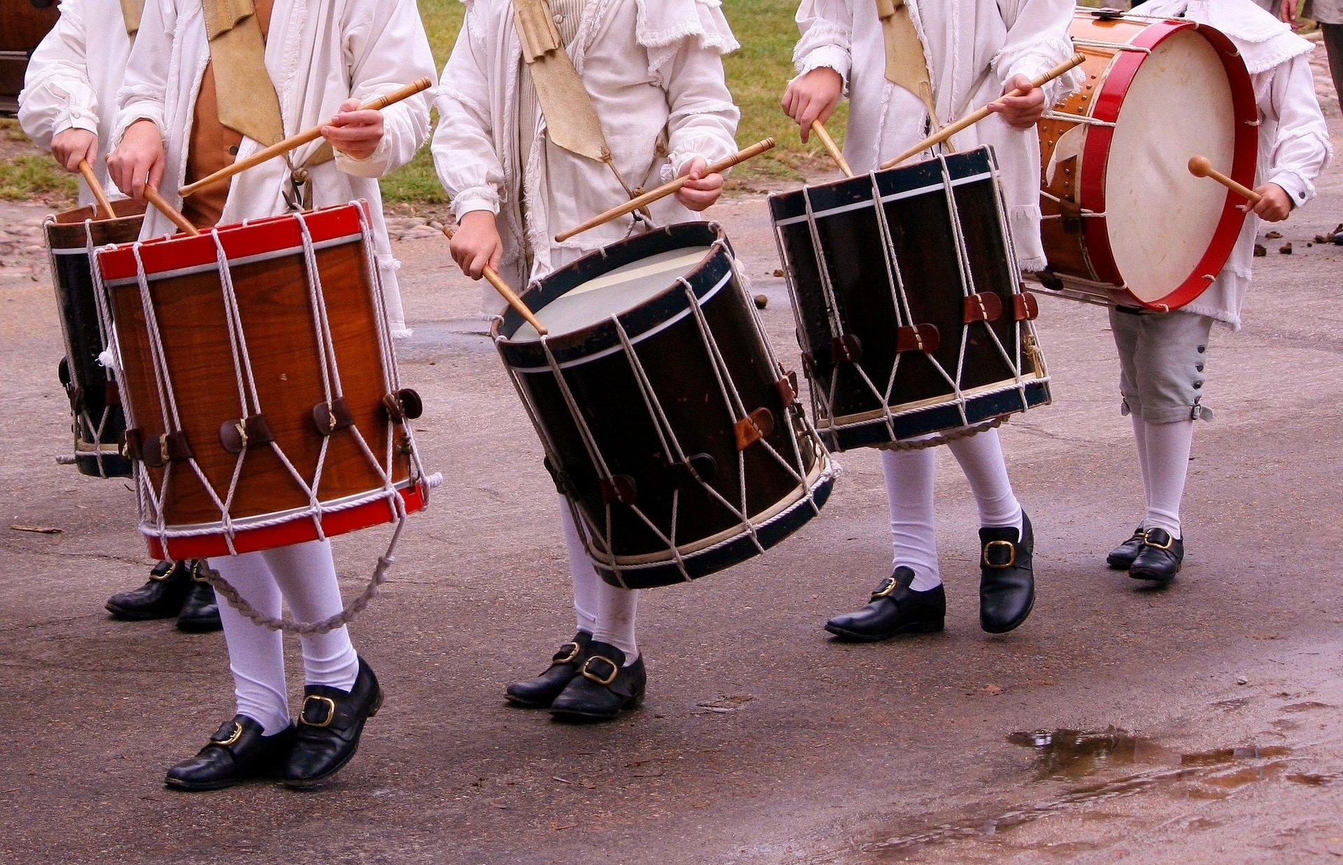 men marching with tom drums and old costumes. their faces are not within the frame of the image