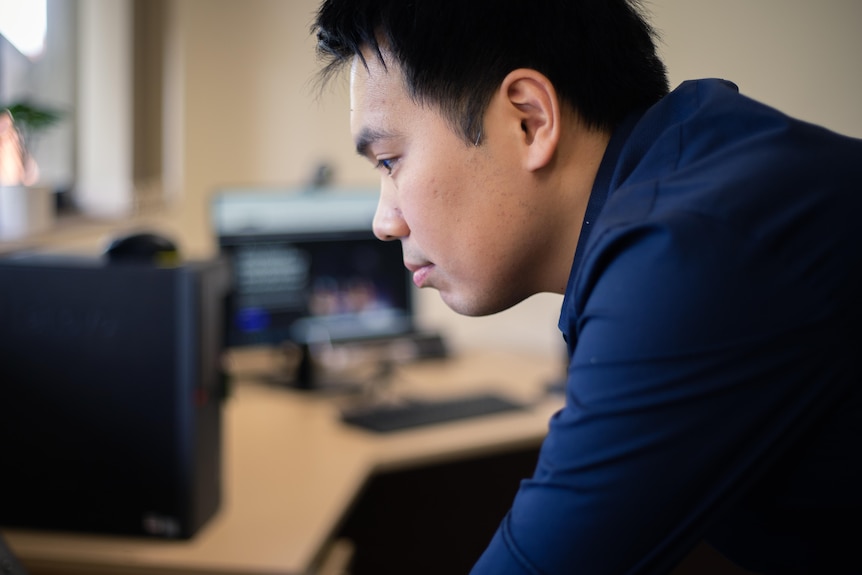 Man with dark blue shirt looks at computer screen.