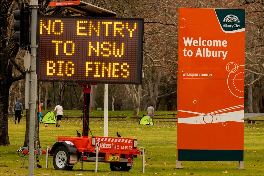 An electronic sign reading 'No entry to NSW big fines' next to 'Welcome to Albury' sign