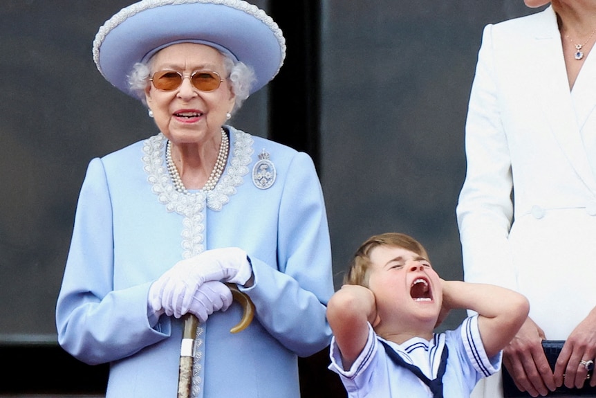 The Queen stands on the palace balcony watching trooping the colour with grandson louis covering his ears and screaming