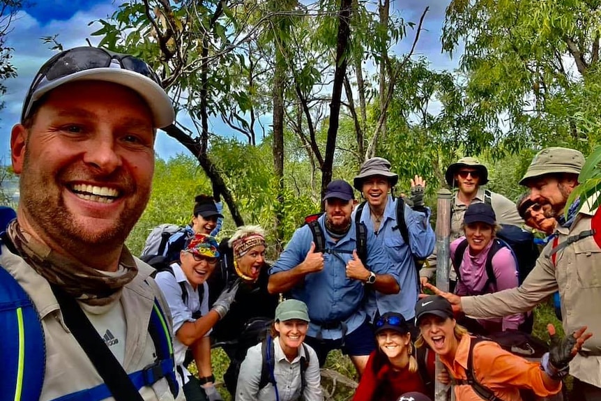 Michael smiling, several hikers behind him, trees and sky behind.