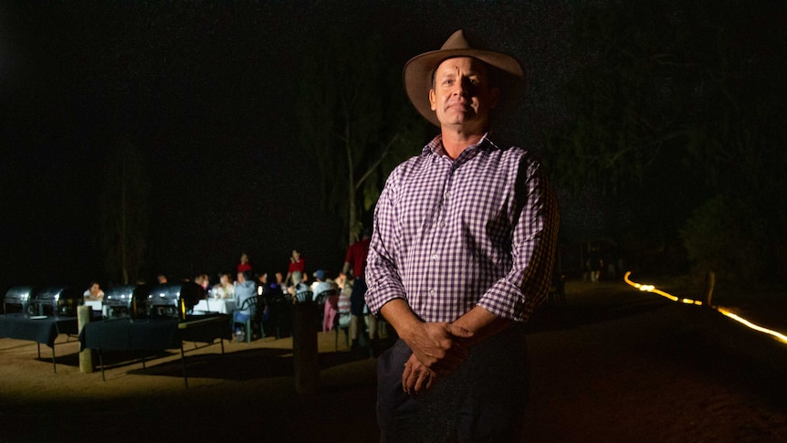 Scott McMillan is wearing a long-sleeved shirt and hat and looks at the camera. Behind him is a tour group.