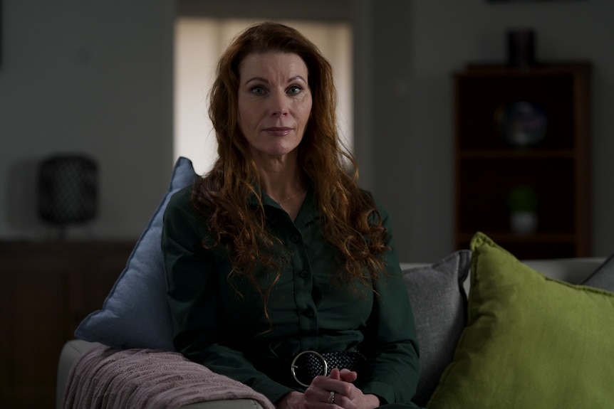 A woman sits on a couch and looks into the camera with a serious expression on her face.