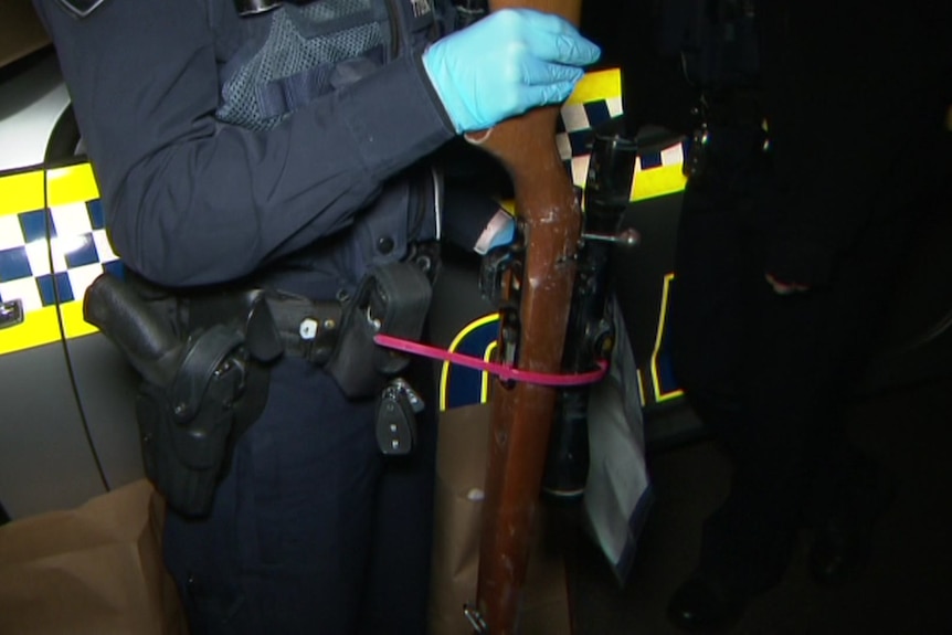 A police officer holds an allegedly stolen rifle.