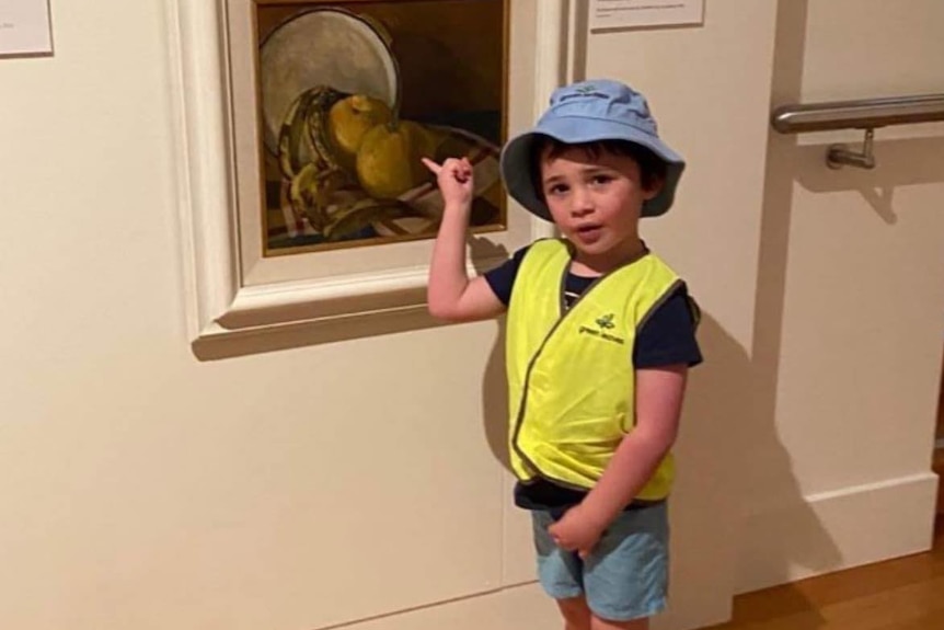 A child in a yellow vest points at a painting in a gallery.