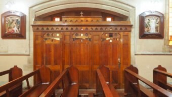 A wooden confessional box sits at the end of a row of pews inside a Catholic church.