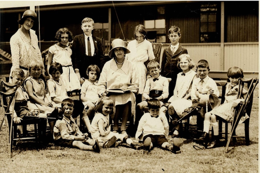 A group of children, some with crutches, sitting around a woman in a black and white photo. 