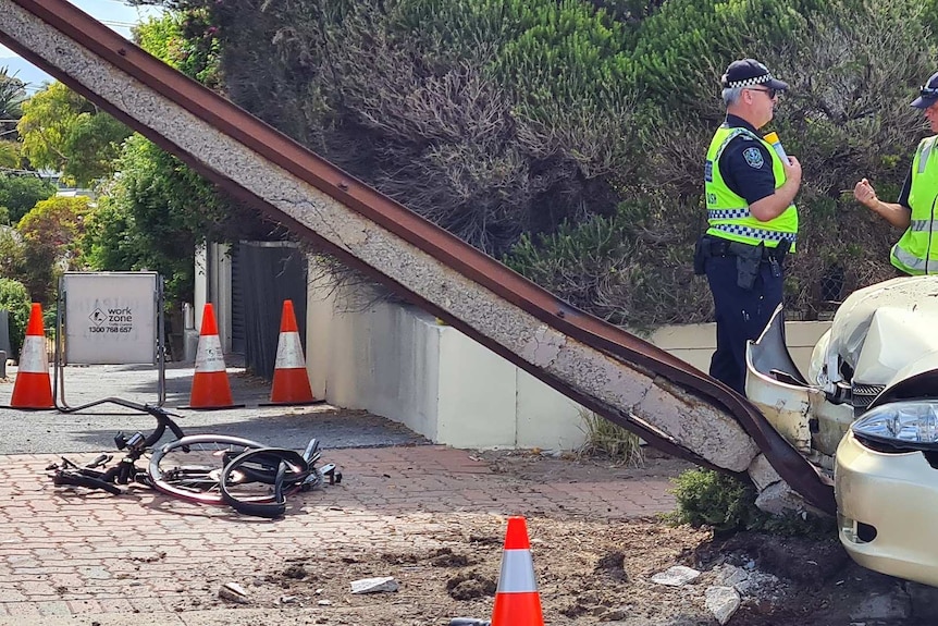 Un vélo mutilé à côté d'une voiture endommagée et d'un poteau Stobie.