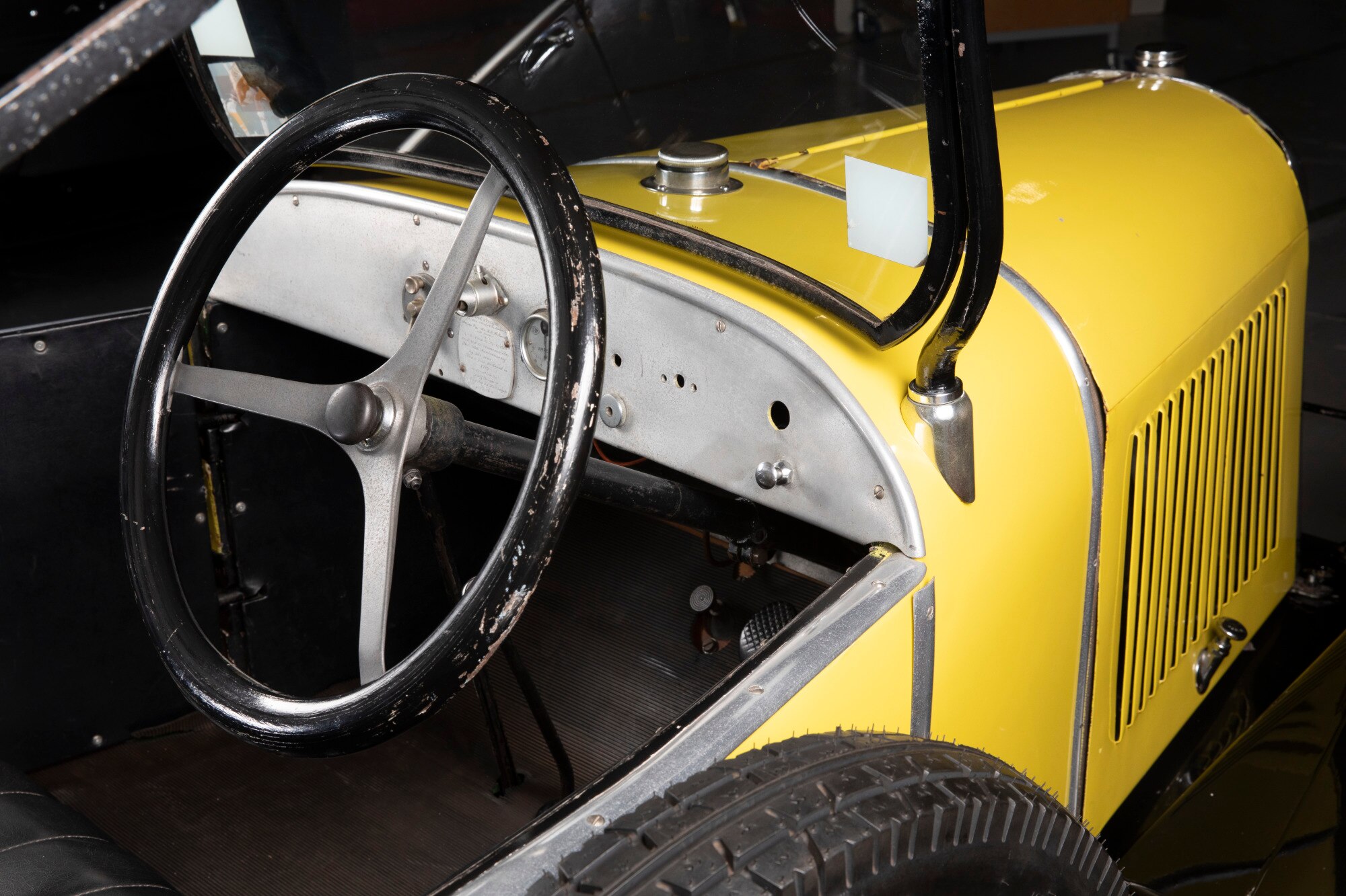 A scuffed black steering wheel of a yellow 1923 Citroën 5CV.
