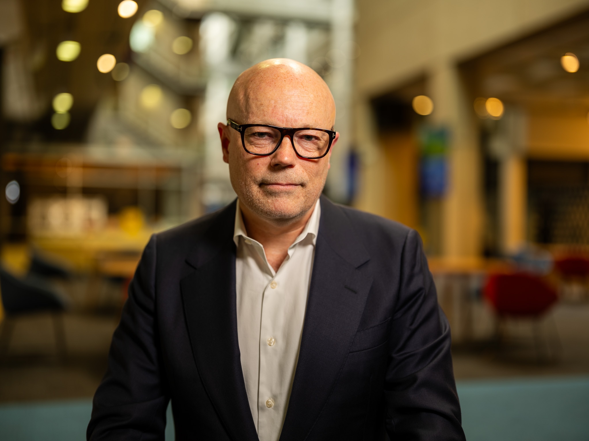 Un hombre con gafas oscuras está sentado pensativamente ante un escritorio.