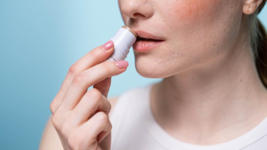 a close up of a woman applying lip balm to her lips
