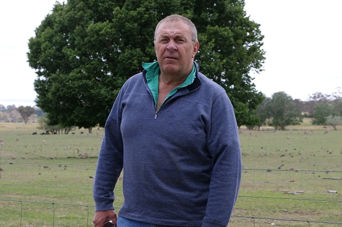 Jock Laurie stands in front a of a green paddock, patting his brown kelpie.