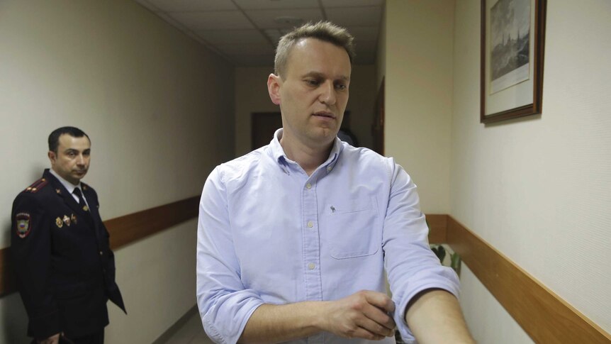 Russian opposition leader Alexei Navalny rolls up his sleeve while walking in a hallway.