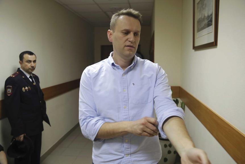Russian opposition leader Alexei Navalny rolls up his sleeve while walking in a hallway.