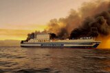 A ferry is on fire with smoke billowing off deck.