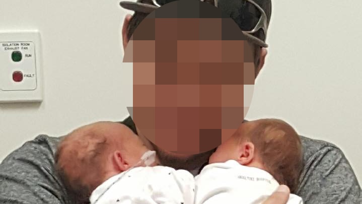 A pixelated photo of the man holding two babies.