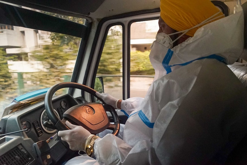 A Sikh Indian man in full PPE behind the wheel of a car