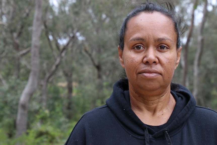 A head and shoulders shot of an Indigenous woman posing for a photo outdoors with trees behind her.