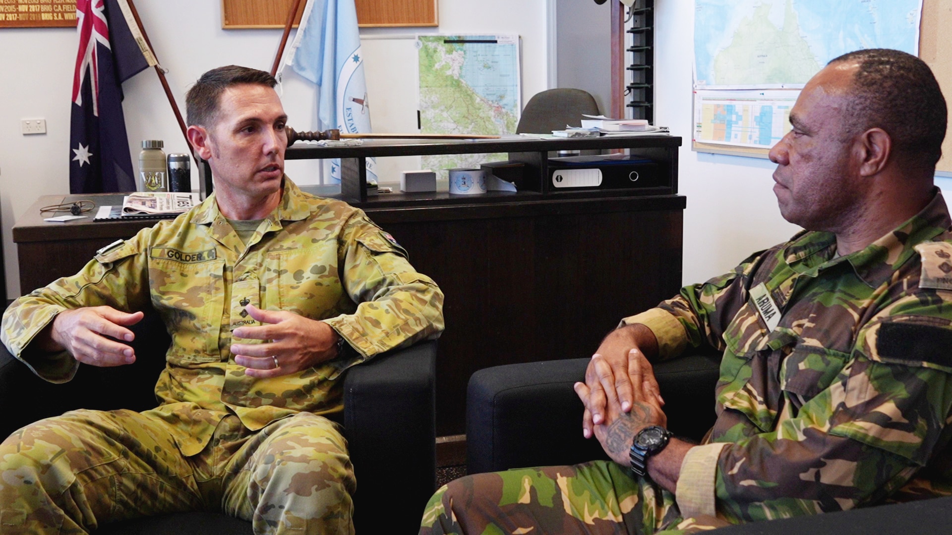 Two defence personnel sit and talk on couches in office.
