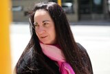 A head and shoulders shot of Carmel Barbagallo outside court weaing a black coat and pink scarf and looking over her shoulder.