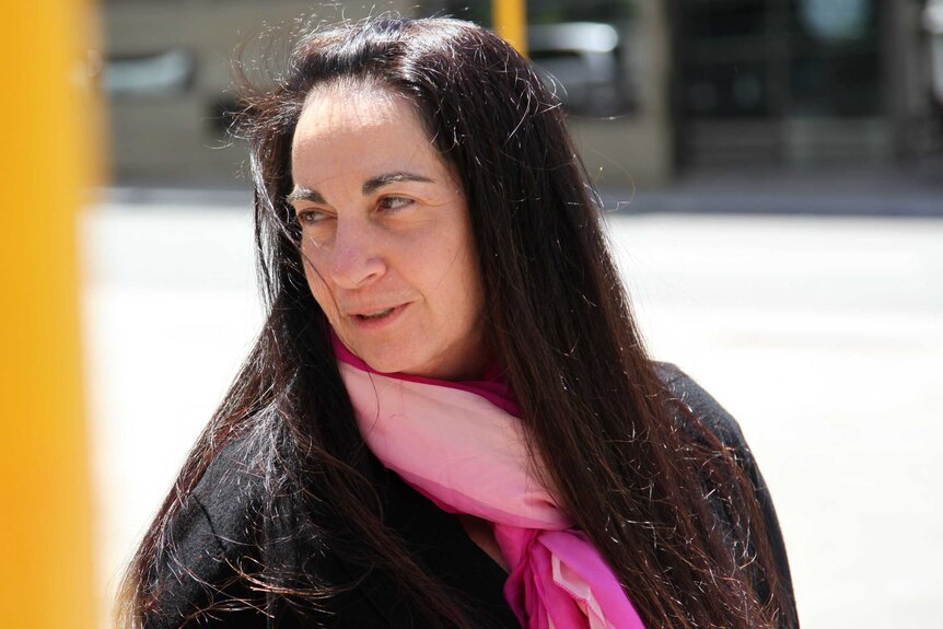 A head and shoulders shot of Carmel Barbagallo outside court wearing a black top and pink scarf.