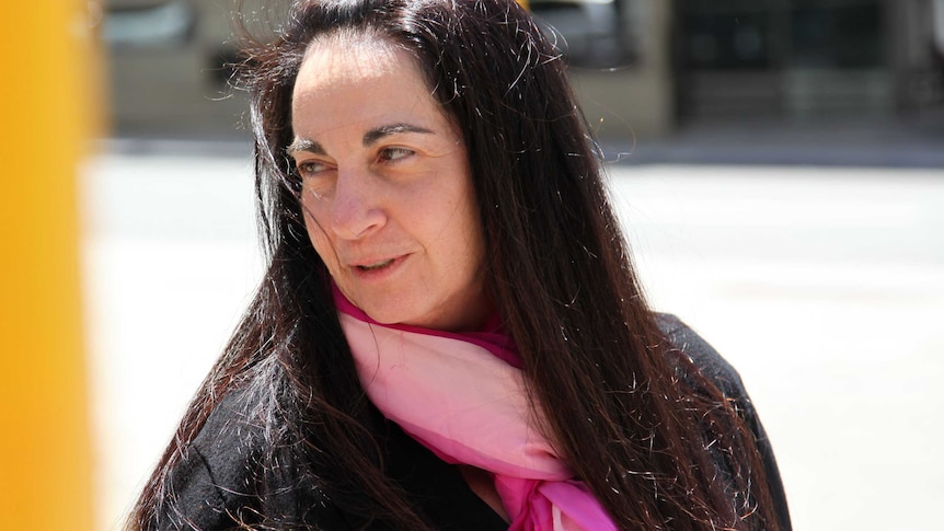 A head and shoulders shot of Carmel Barbagallo outside court weaing a black coat and pink scarf and looking over her shoulder.