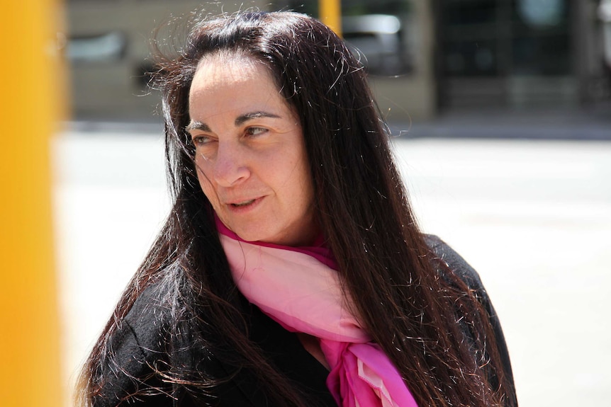 A head and shoulders shot of Carmel Barbagallo outside court wearing a black top and pink scarf.