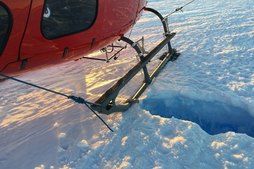 A helicopter, landed on a faint line in the snow, with a hole in it where David Wood fell through.