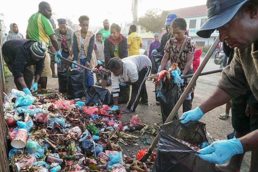 People pick up rubbish with shovels and put it in rubbish bags.