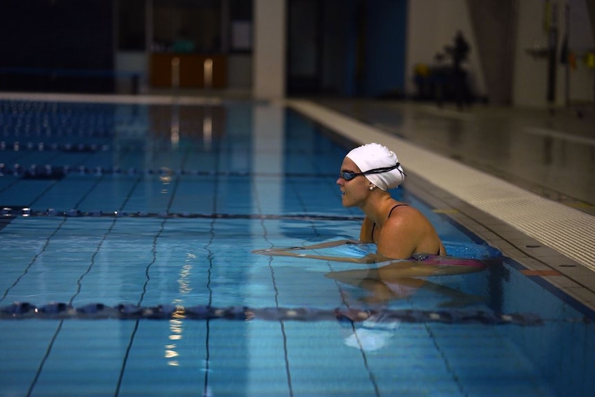 A woman in a white swimming cap and goggles alone in a pool